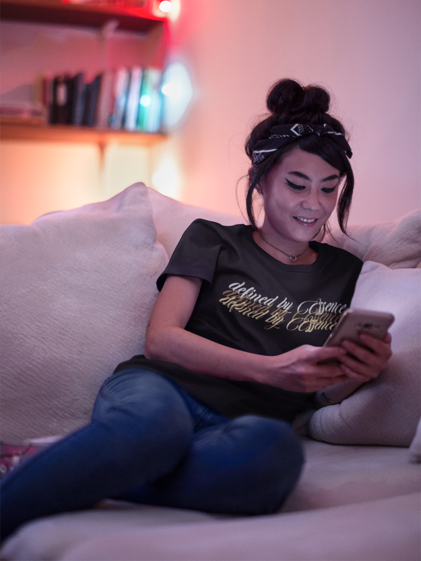Women wearing black 3d Defined By Essence T- Shirt with multilayering wording sitting on the couch while on the phone..