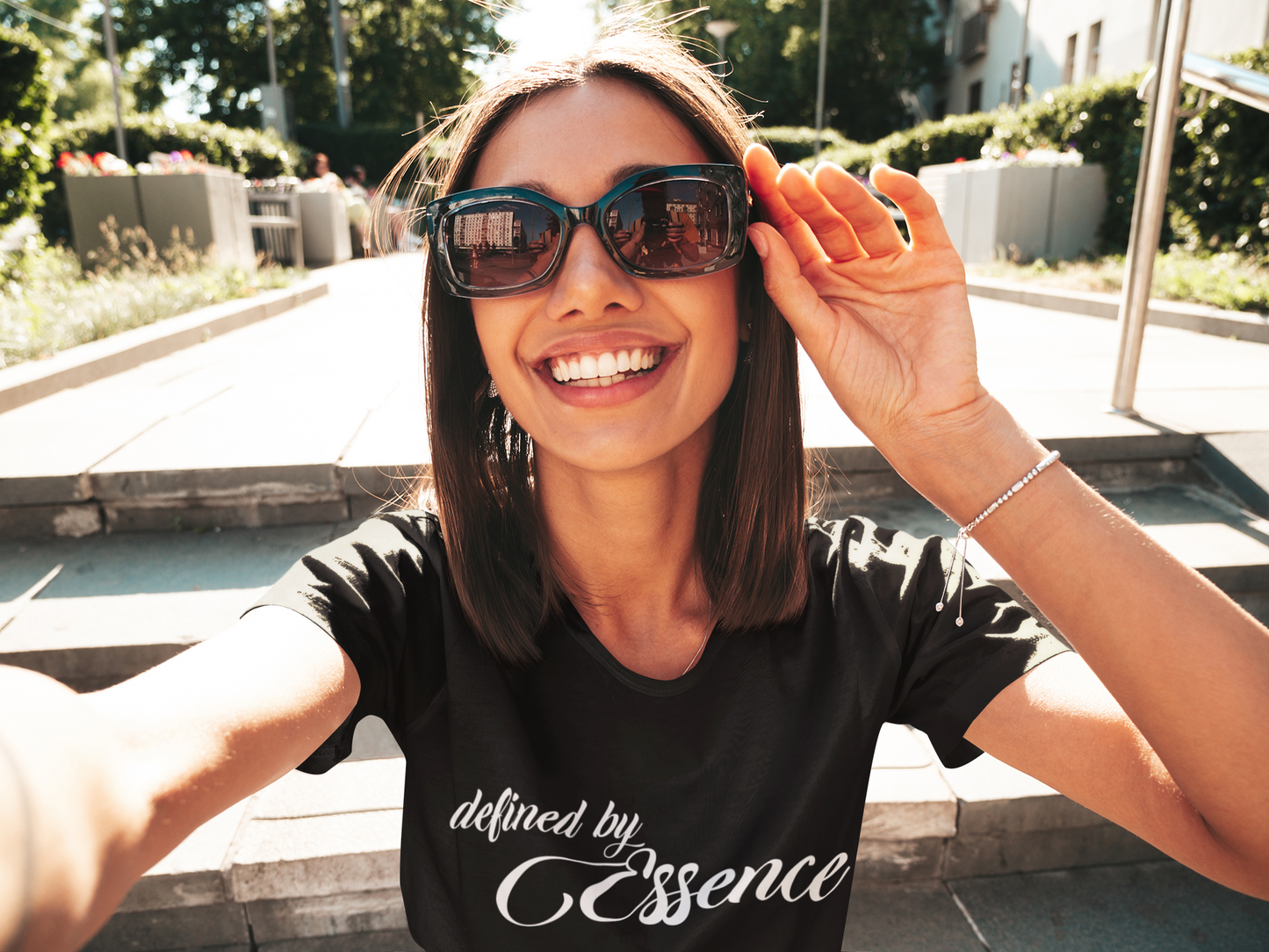 Women wearing a black signature Defined By Essence T-Shirt with white writing, outside wearing sunglasses