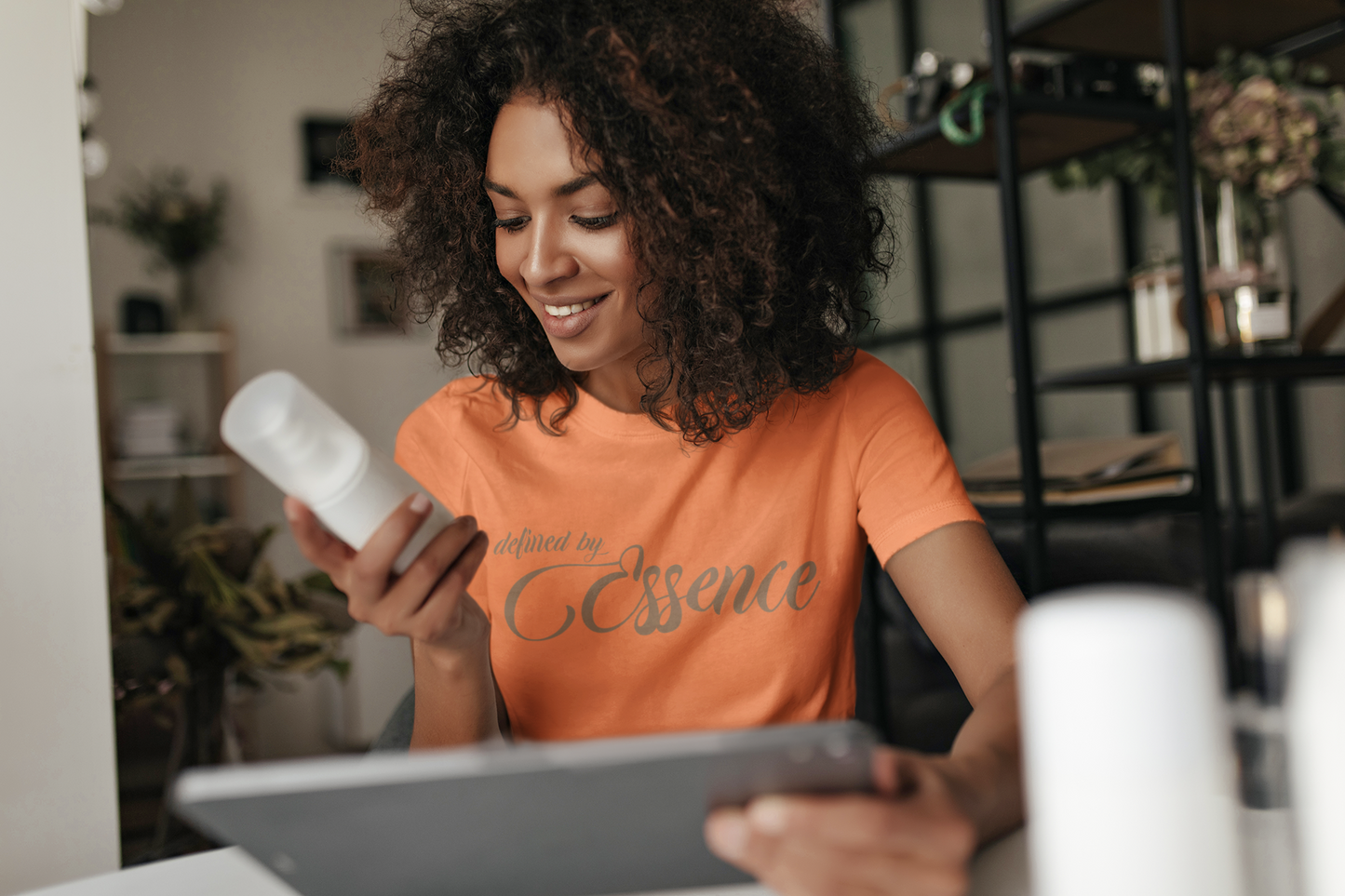 Women wearing a orange signature Defined By Essence  t-shirt with beige writing, looking at a product.