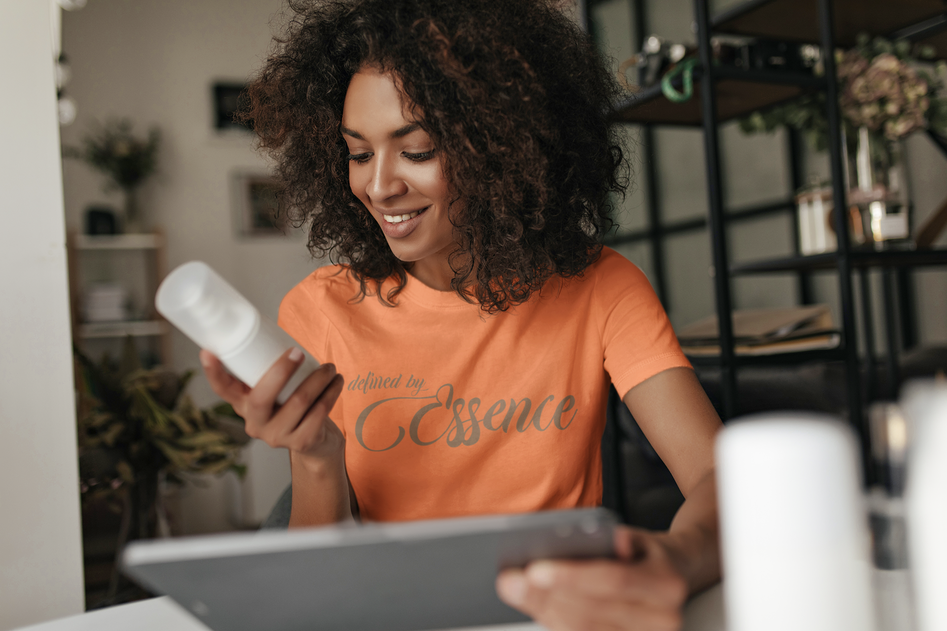 Women wearing a orange signature Defined By Essence  t-shirt with beige writing, looking at a product.